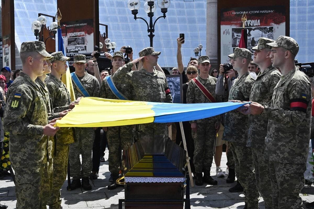 Des soldats ukrainiens tiennent un drapeau au-dessus d'un cercueil.