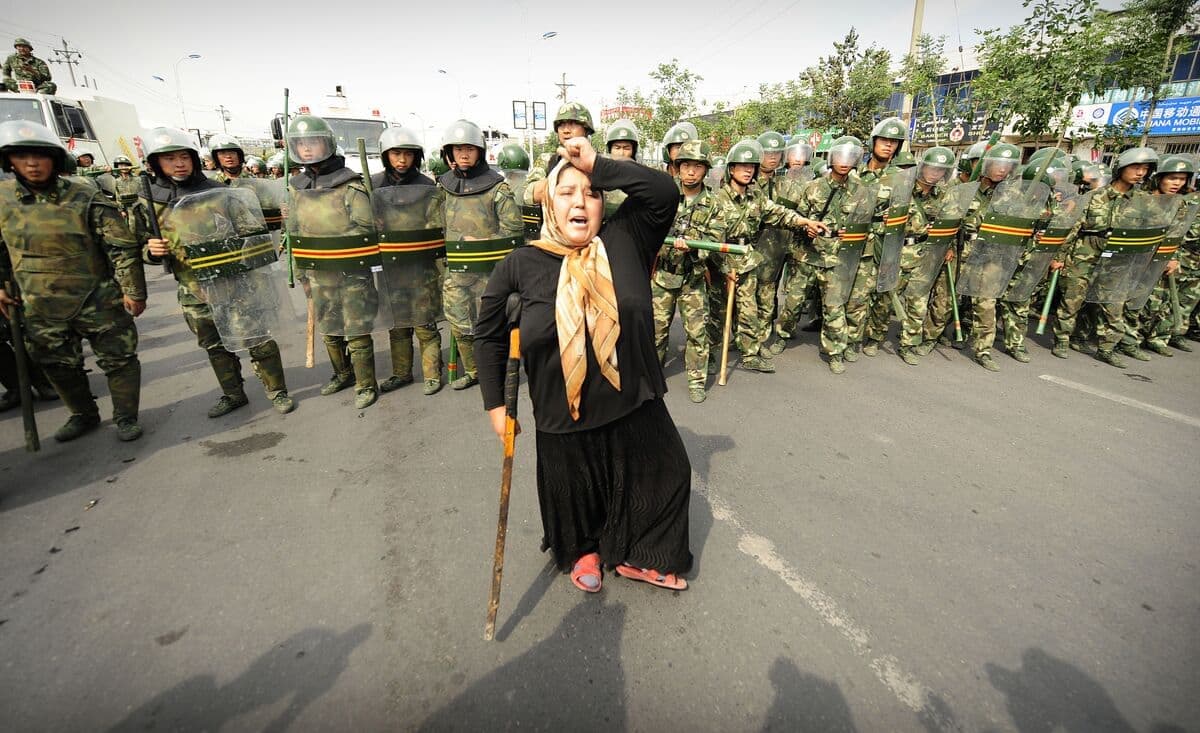 Cette photo d'archive prise le 7 juillet 2009 montre la police anti-émeute chinoise regardant une femme musulmane ouïghoure manifester à Urumqi dans la province du Xinjiang, à l'extrême ouest de la Chine