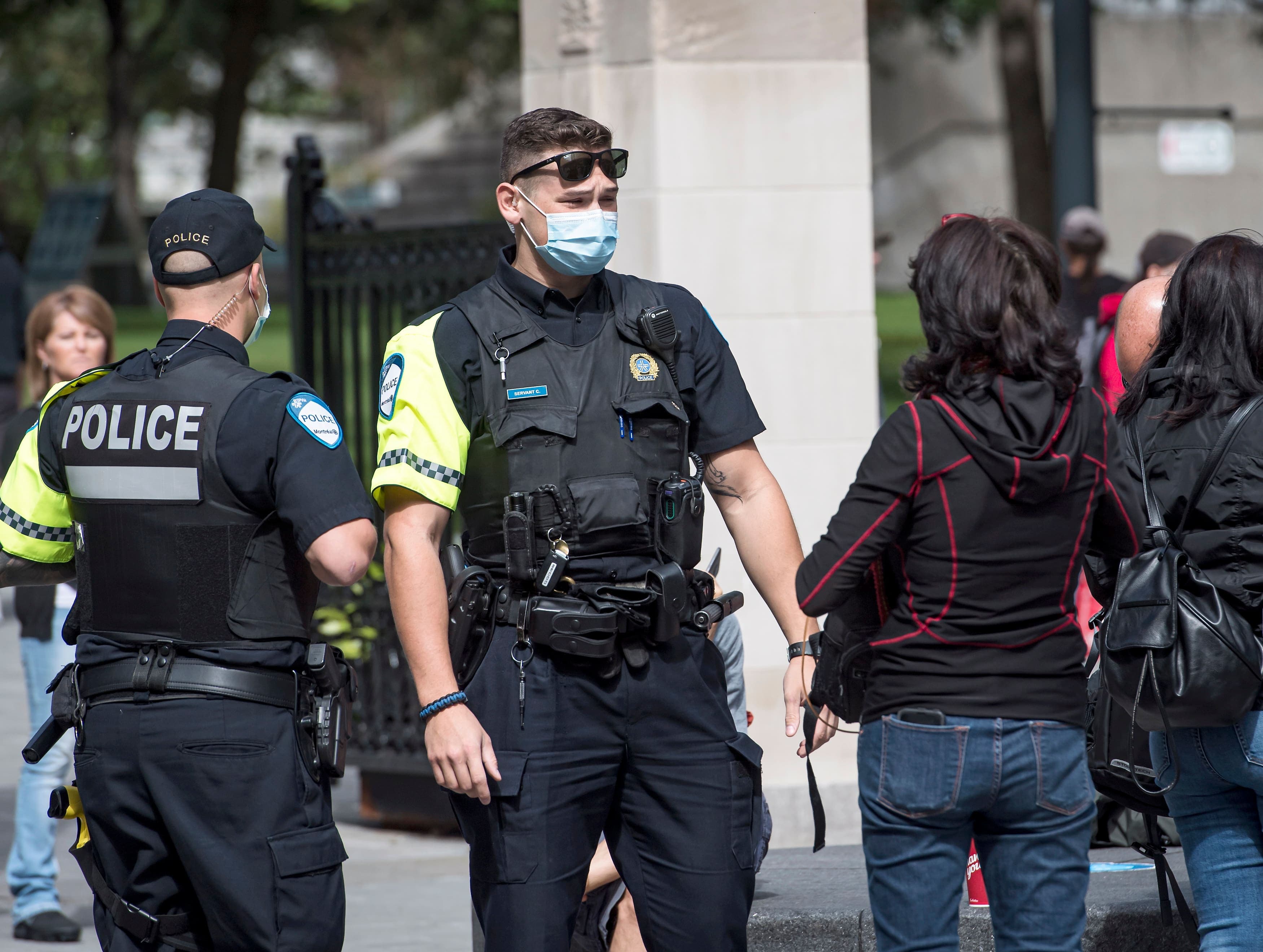 Deux policiers portant le masque discutent avec une femmes en marge de la manifestation contre les mesures sanitaires, à Montréal. Depuis hier, les agents peuvent distribuer des constats d’infraction à ceux qui ne portent pas le masque à l’intérieur des lieux publics fermés.