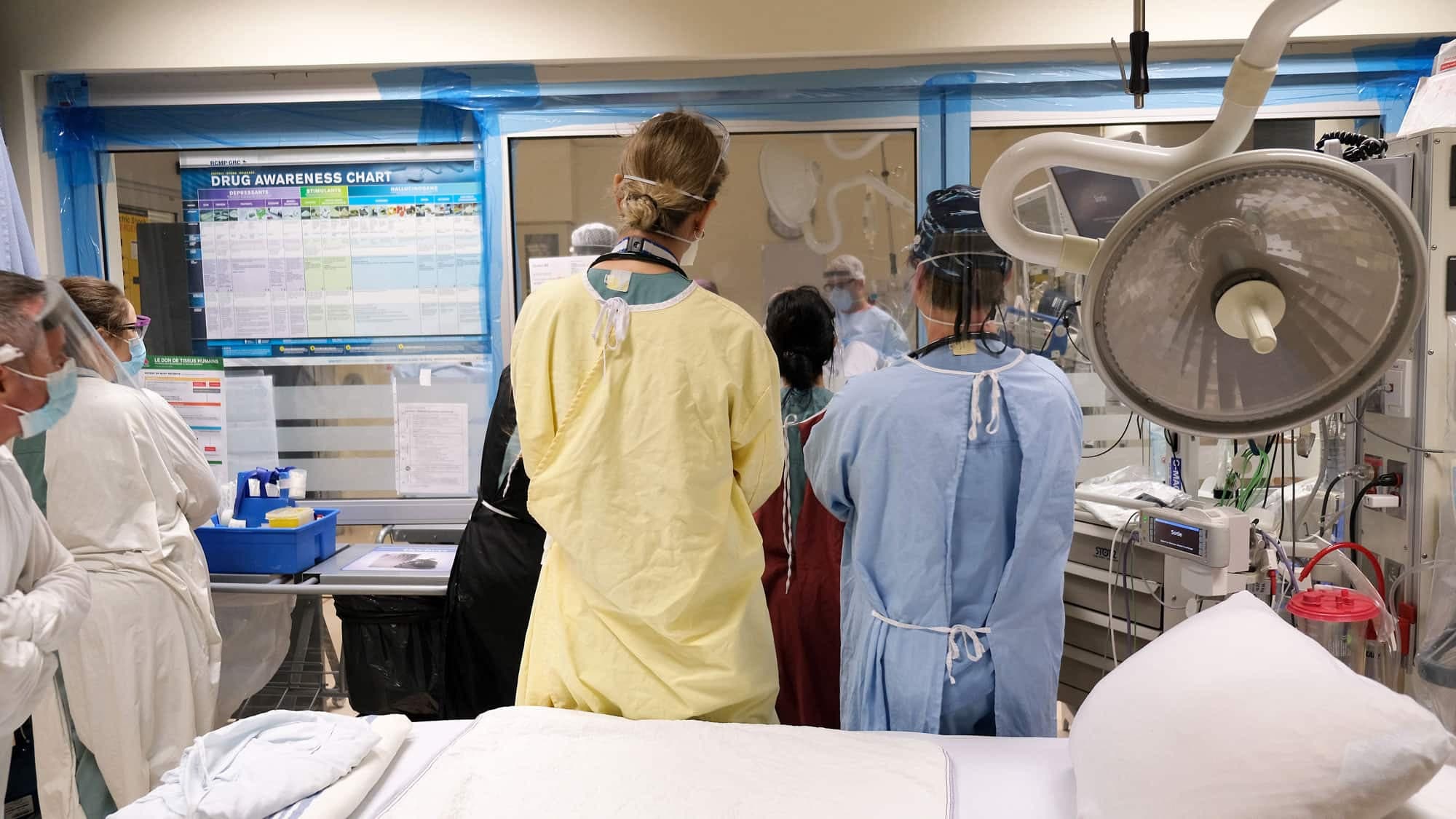 Des soignants de l’urgence surveillent un patient en détresse respiratoire par la fenêtre d’une chambre adjacente, pour réduire les risques d’infection.