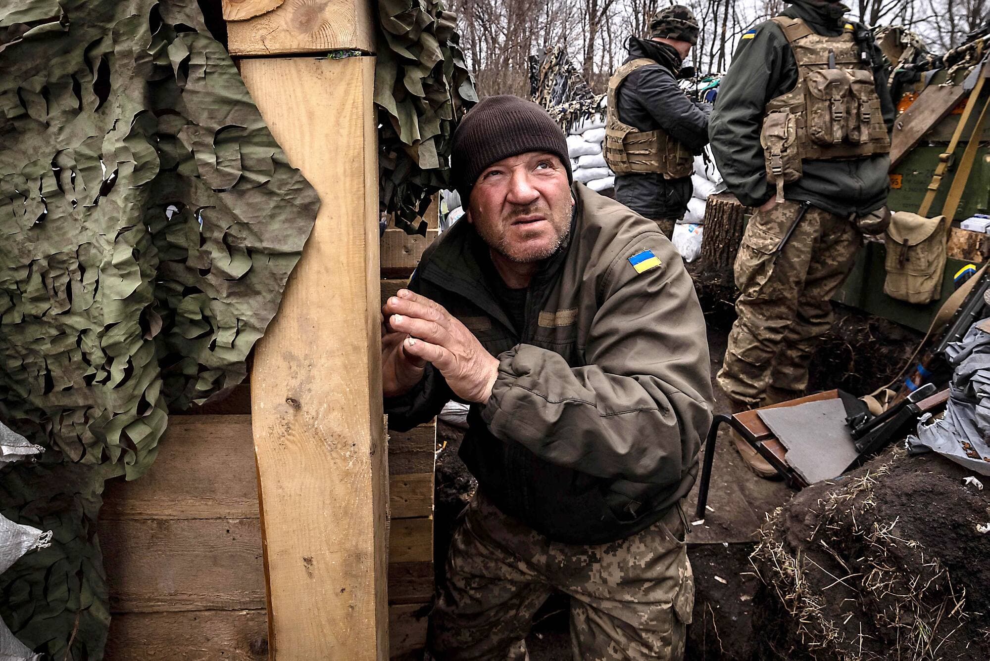 Son drapeau de l’Ukraine bien visible à l’épaule gauche, un soldat garde un œil sur l’offensive russe, accroupi dans la tranchée.